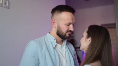 Romantik sevgililer günü çifti, Minimalist iç mekanlarda hafif mor ortam aydınlatmasıyla aydınlanan kadın ve erkek şefkatle kucaklaşıyor..