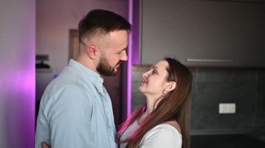 Romantik sevgililer günü çifti, Minimalist iç mekanlarda hafif mor ortam aydınlatmasıyla aydınlanan kadın ve erkek şefkatle kucaklaşıyor..