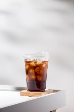Iced americano in a plastic mug on a white table in the cafe.	
