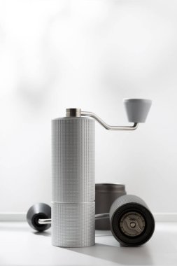 Vertical photo of light gray manual coffee grinder on white table.