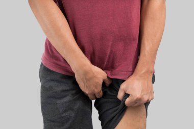 Asian men grab or cover his crotch because wanting to urinate against gray background.