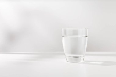 Bardaktaki saf su beyaz ahşap masanın üzerinde..