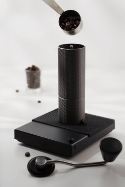 Kahve çekirdeklerini siyah dijital ölçekte öğütücüye atmak için paslanmaz çelik kaşık kullanın..