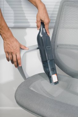 Adam ofisteki gri sandalyeleri temizlemek için kablosuz bir elektrikli süpürge kullanıyor..
