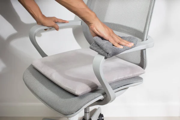 A man used a microfiber cloth to clean a gray chair armrest in the office.