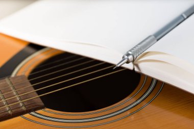 Kahverengi bir kalem ve koyu kırmızı bir defter akustik bir gitara yerleştirilir..