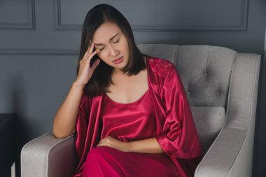 Kırmızı gecelikli kadın, tatil köyünün yatak odasında baş ağrısıyla oturuyor..
