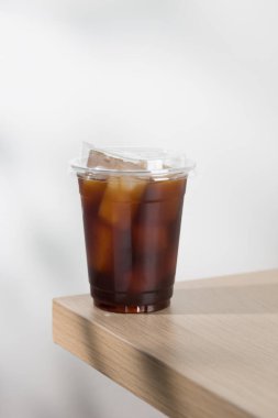 Şeffaf bir fincanda sergilenen ferahlatıcı buzlu americano, yumuşak odaklı arka planı olan ahşap bir masada sergileniyor..