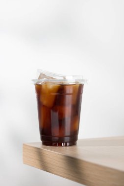 Şeffaf bir fincanda sergilenen ferahlatıcı buzlu americano, yumuşak odaklı arka planı olan ahşap bir masada sergileniyor..