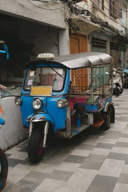 Parlak mavi bir tuk-tuk, Tayland 'ın eşsiz sokak taşımacılığını somutlaştıran desenli bir yola park etmiş..