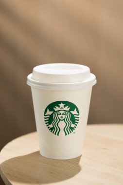 Bir Starbucks kahve fincanı ahşap bir masanın üzerinde, simgesel yeşil ve beyaz logoları sergiliyor..