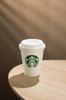 Bir Starbucks kahve fincanı ahşap bir masanın üzerinde, simgesel yeşil ve beyaz logoları sergiliyor..