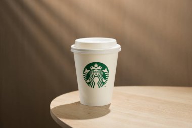 Bir Starbucks kahve fincanı ahşap bir masanın üzerinde, simgesel yeşil ve beyaz logoları sergiliyor..