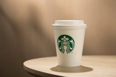 Bir Starbucks kahve fincanı ahşap bir masanın üzerinde, simgesel yeşil ve beyaz logoları sergiliyor..