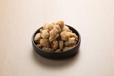 Popüler bir Kuzey Tayland yemeği olan Kaeb Moo veya Çıtır domuz derisi küçük siyah bir tabakta servis edilir. Açık ahşap masa domuz derisinin altın-kahverengi rengiyle çelişiyor..