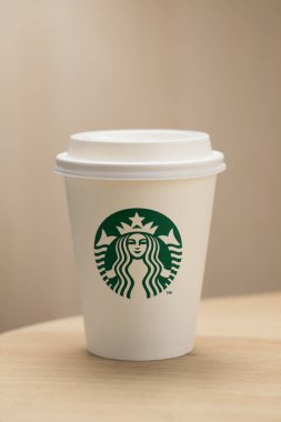Bir Starbucks kahve fincanı ahşap bir masada oturur. Markaların ikonik yeşil ve beyaz logolarını gösterir.