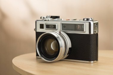 A classic silver film camera encased in black rubber, utilizing a rangefinder focusing system and a 35mm manual focus lens, displayed on a wooden table. clipart