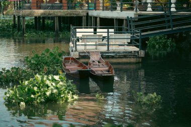 Ahşap tekneler nehir kenarındaki bir evin yanında dinlenirken sakin sahneler ortaya çıkıyor ve yerel topluluktaki günlük nehir yaşamının dingin ritmini vurguluyor..