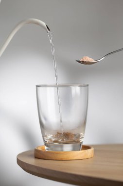 A spoon with himalayan salt beside a drinking glass as hot water pour inside, highlighting natural mineral hydration and healthy lifestyle.