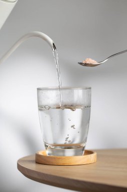 A spoon with himalayan salt beside a drinking glass as hot water pour inside, highlighting natural mineral hydration and healthy lifestyle.