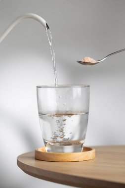 A spoon with himalayan salt beside a drinking glass as hot water pour inside, highlighting natural mineral hydration and healthy lifestyle.