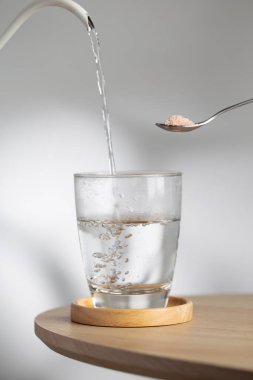 A spoon with himalayan salt beside a drinking glass as hot water pour inside, highlighting natural mineral hydration and healthy lifestyle.