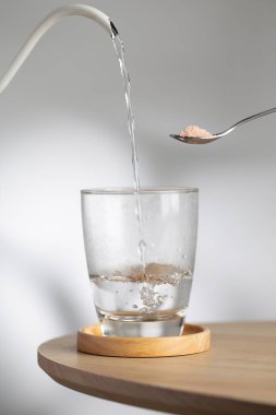 A spoon with himalayan salt beside a drinking glass as hot water pour inside, highlighting natural mineral hydration and healthy lifestyle.