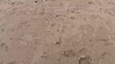 Kumlu sahil manzarası, yumuşak kum ve kamera kaymalarında Sur Sahili 'nin su dalgalarına çarpan çok sayıda ayak izi ve desenler gösteriyor.