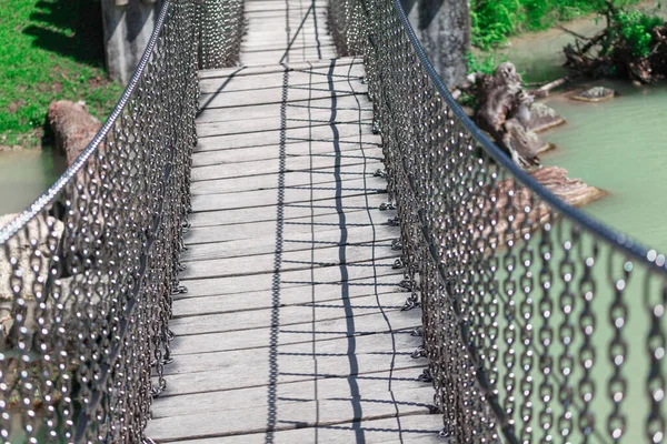 Footbridge over the river . Pedestrian bridge made by chains and wooden planks . Hanging walkway