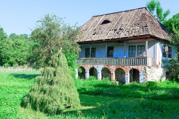 Stack of Grass Near Traditional Rustic House . Old Country House with Straw Roof