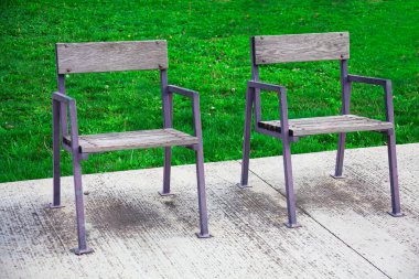 Parktaki ahşap sandalyeler yeşil çimenli beyaz ahşap bir zeminde. İki boş koltuk.
