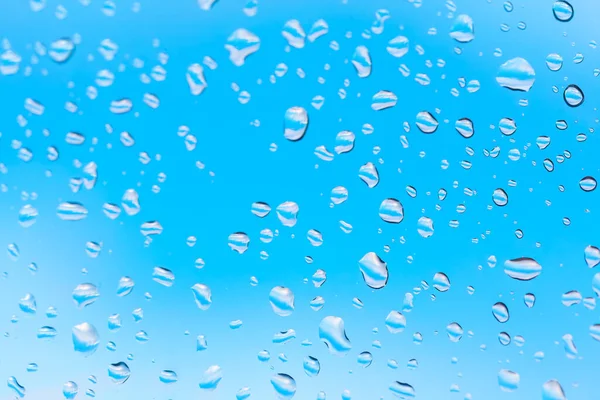 Macro shot of water droplets clinging to a glass surface . Water drops at window glass against blue sky