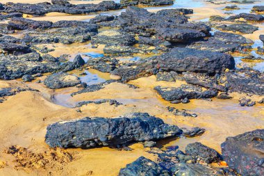 Engebeli volkanik kayaların manzarası sakin bir kumsalın yumuşak, altın kumlarıyla çelişiyor.