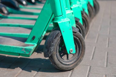 Park halindeki elektrikli scooter 'lar bir sokakta sıraya dizilmiş. Park halindeki elektrikli scooterların tekerlek seçici odağı