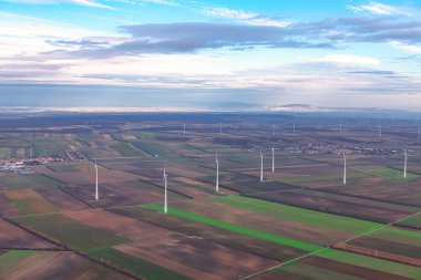 Rüzgar çiftliği ve tarım arazileri yukarıdan görünüyor. Rüzgar türbinleri temiz enerji üretmek için rüzgarın gücünden faydalanıyor.