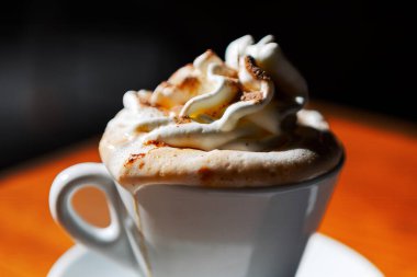 Kapuçino, ahşap bir masada beyaz bir fincanda çırpılmış krema.