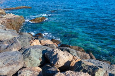 Güneşli bir günde kayalık sahil ve turkuaz su. Kıyıdaki kayalar derin mavi denizle çelişiyor.