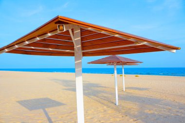 Deniz kenarındaki kumlu sahilde tahta şemsiyeler. Mükemmel yaz tatili 