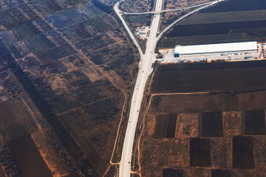 Çevresi tarımsal tarlalarla çevrili, hareket halindeki bir otoyolun havadan görüntüsü.
