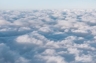 Bir uçak penceresinden pofuduk beyaz bulutların havadan görünüşü. Uçakta uçarken gökyüzü görüntüsü