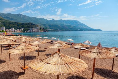 Karadağ 'daki Becici plajı. Kumsal sahnesi, renkli şemsiyeler ve kumdaki şezlonglar.