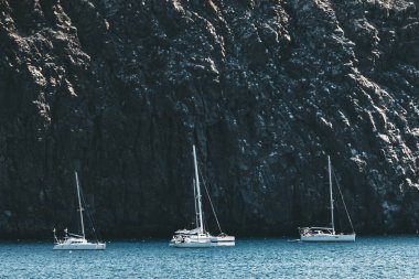 Okyanus kıyısında görkemli kayalıklara doğru yelken açan yatlar. Harika bir yat gezisi.