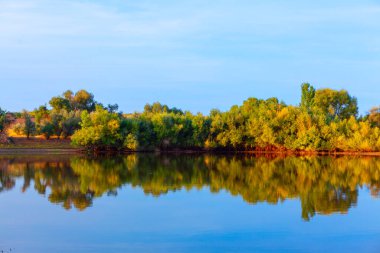 Bereketli ağaçlarla çevrili sakin bir göl. Gökyüzünü yansıtan berrak su.
