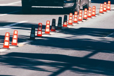 Kırmızı trafik konileri sıraya dizilmişti yolda. Araba koni dolu bir caddede manevra yapıyor. Külahlar sıraya dizilir, bazıları kameraya daha yakın, bazıları ise daha uzaktadır.