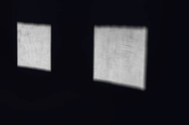 Loş aydınlatılmış bir odada güneş ışığı iki kare pencereden içeri doğru yayılıyor. Üzerinde gölge olan iki beyaz kare.