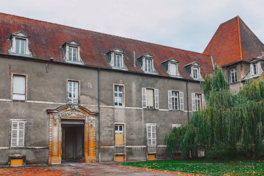 Kırmızı çatılı ve beyaz çizgili büyük bir bina. Binanın bir sürü penceresi ve geniş bir kemer yolu var. Bina eski ve terk edilmiş görünüyor.
