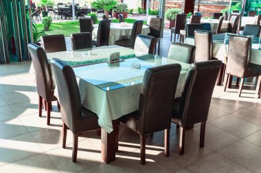 Birçok sandalyeyle çevrili büyük bir masası olan restoran. Masa beyaz bir bez ile kaplı ve sandalyelerin hepsi kahverengi.