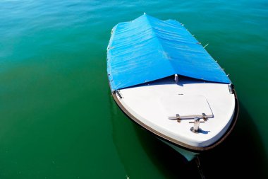  Üzerinde mavi muşamba olan tekne suyun içinde duruyor. Tekne küçük ve üstü beyaz.