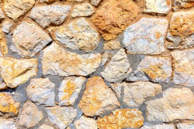 Bir sürü dokusu olan taştan yapılmış bir duvar. Duvar birçok farklı boyutta kayalardan yapılmıştır ve pürüzlü, pürüzlü bir yüzeyi vardır. Duvar eski görünüyor ve kırsal bir alanı var.