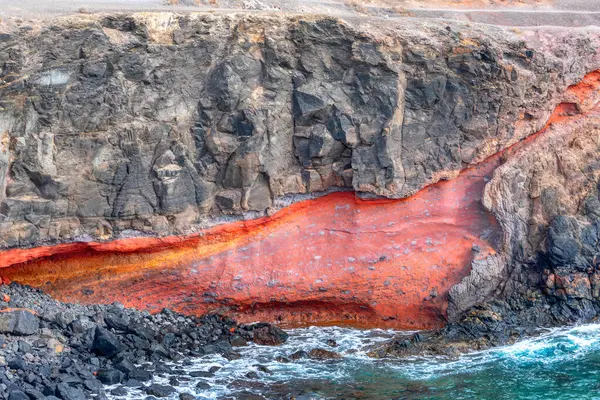 Stock image Cliff with a red flow of water running down it. Majestic rock formation overlooking the ocean